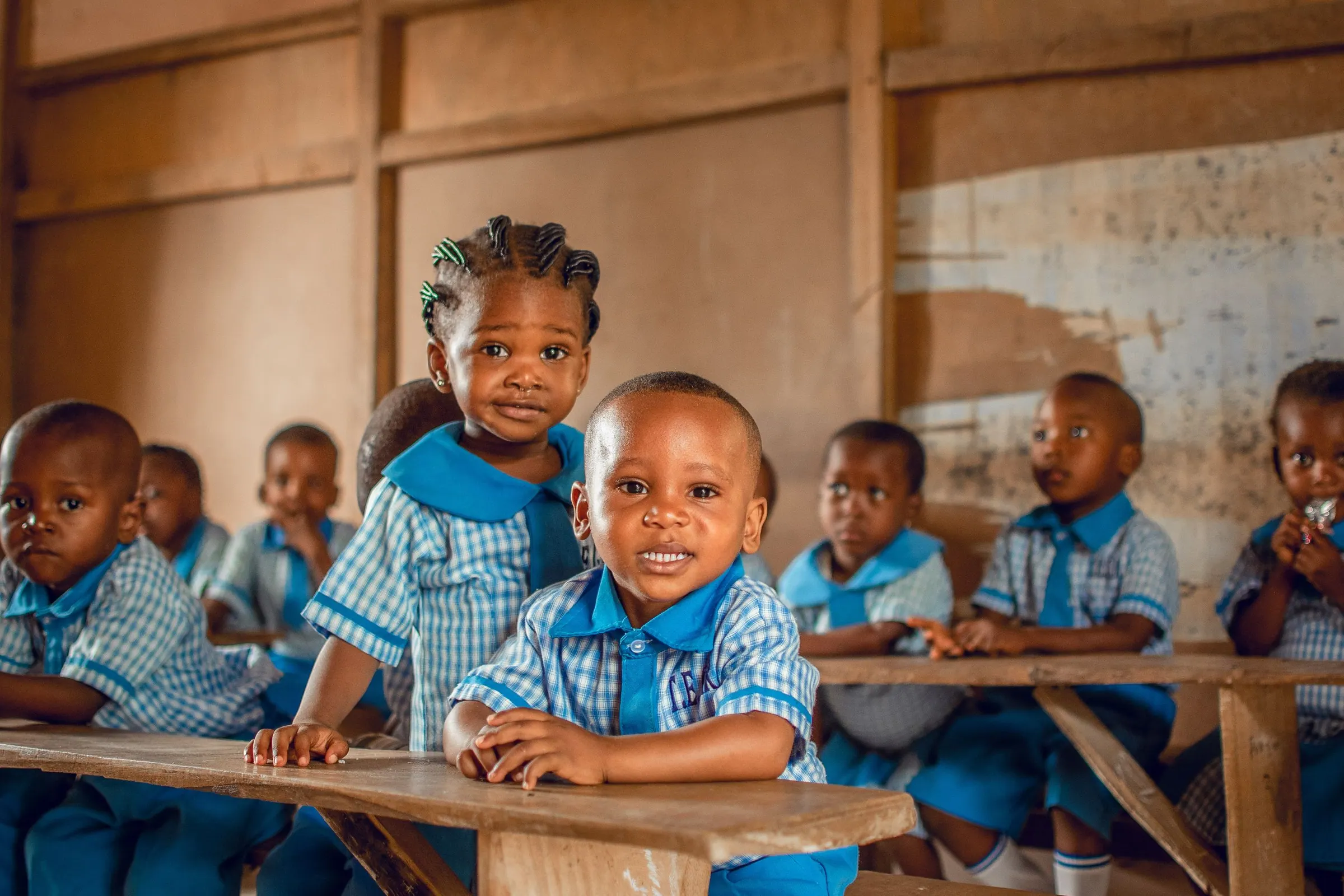 Young pupils in blue uniforms smiling at their classroom desks