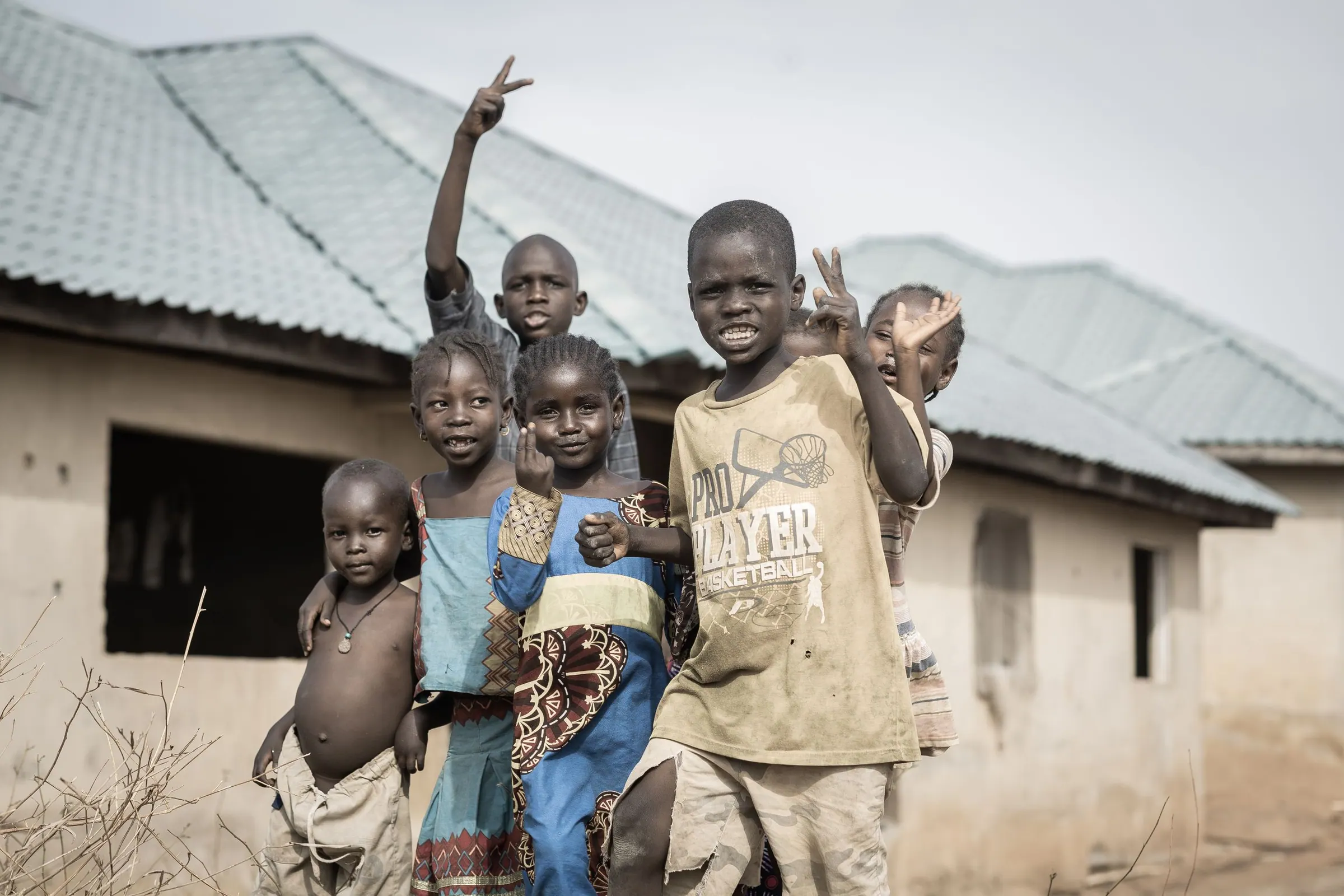 A group of children waving outside their homes in a village
